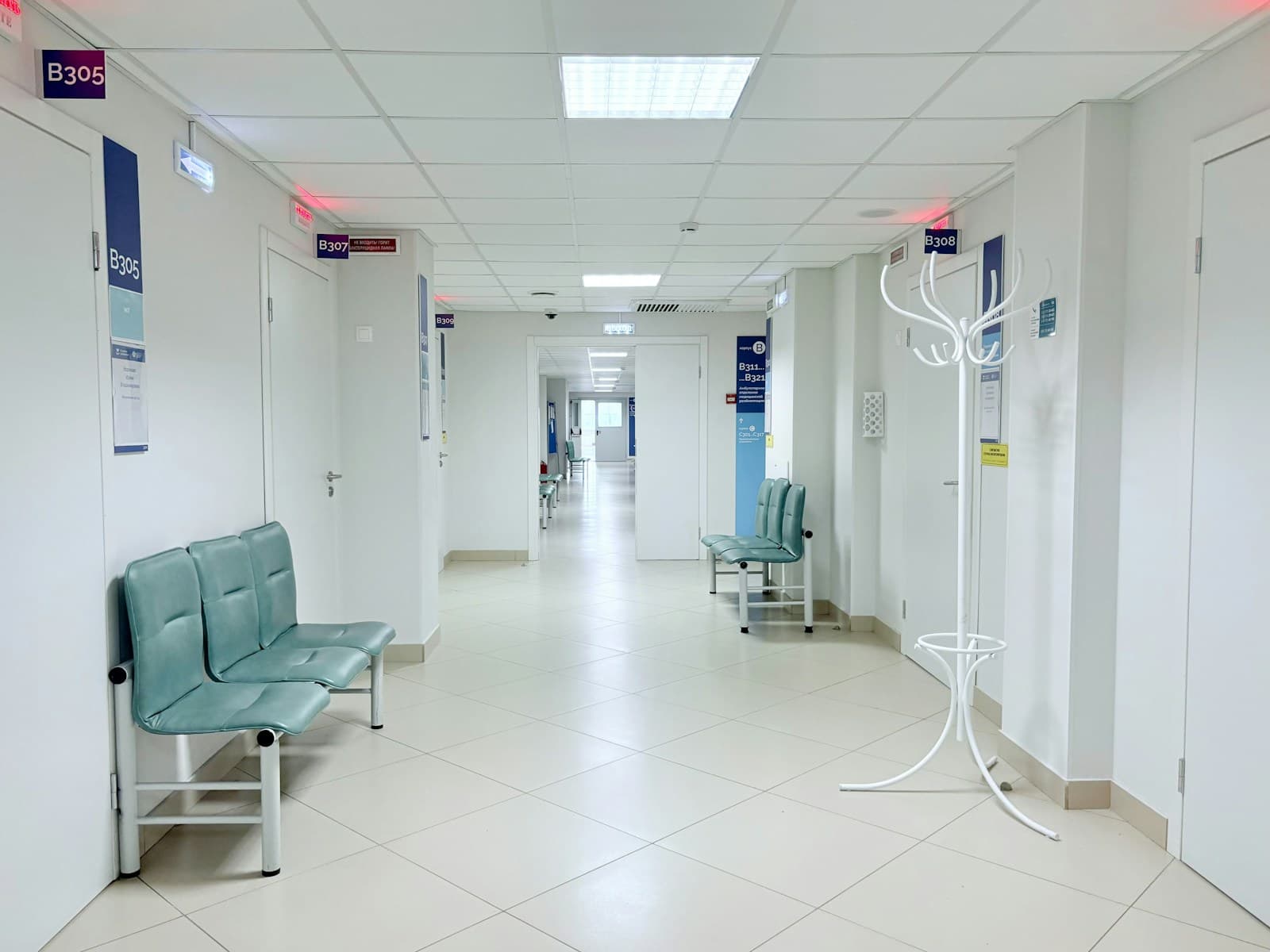 A bright clinical corridor with consultation rooms and waiting seats